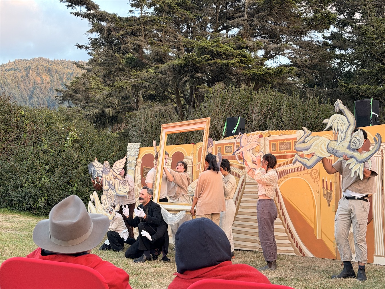 Puppeteers move framed paintings and winged puppets across the ornate painted opera-house set while the fly actor kneels at left.