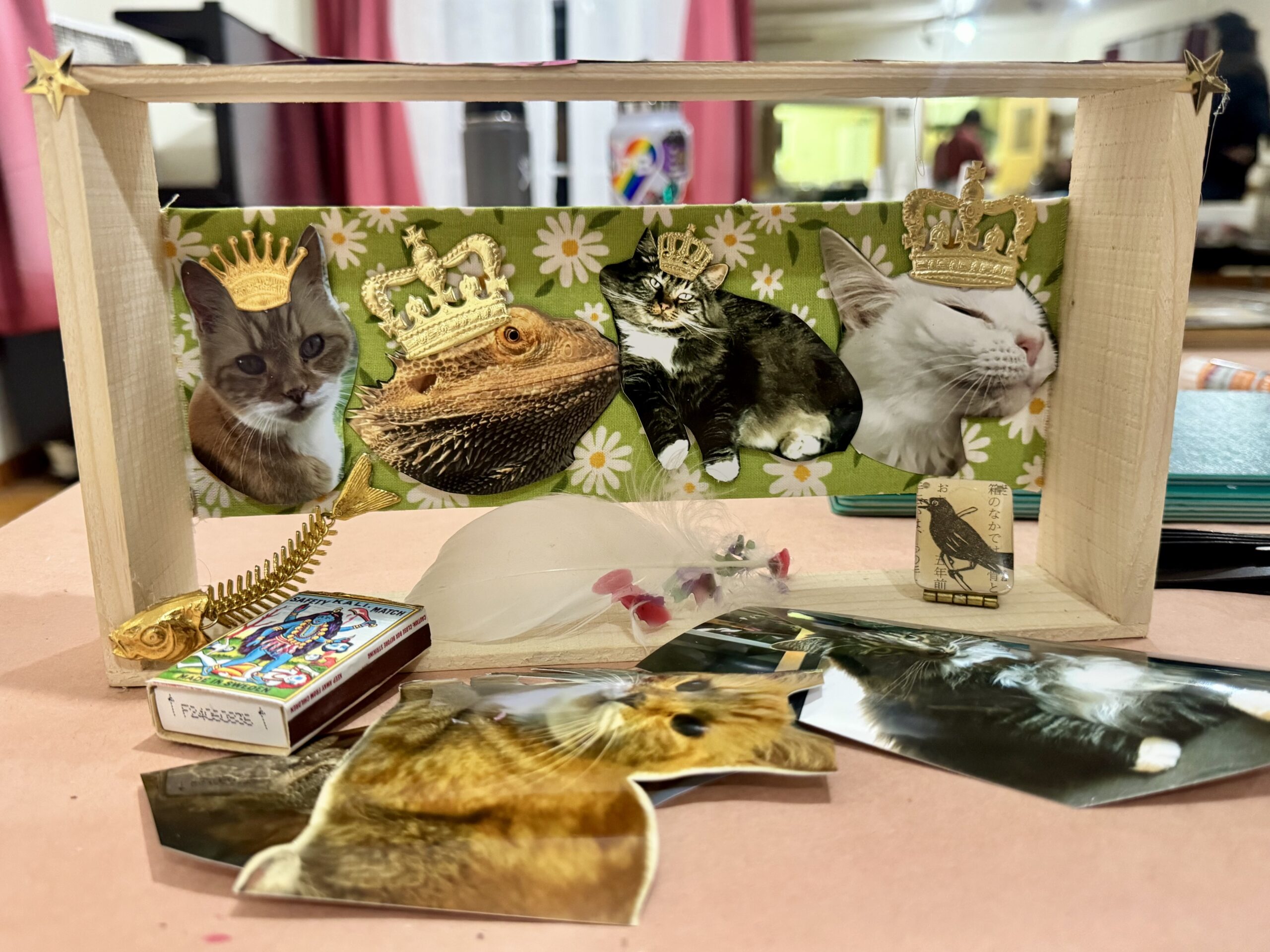 A closer view of the crowned-pets shadow box with a matchbox and loose cutout photos on the table in front.