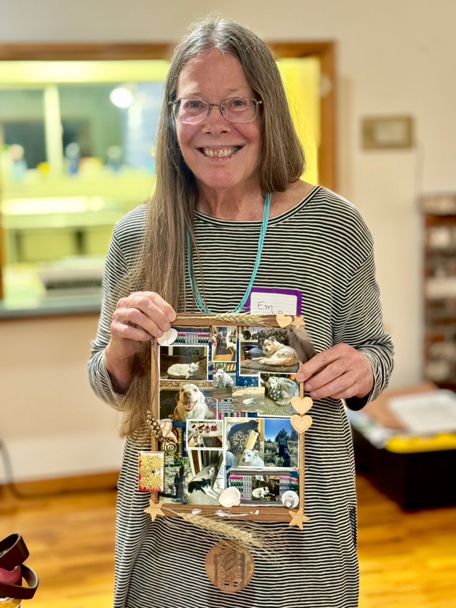 A participant smiling and holding a framed collage of dog photos decorated with wheat, a feather, and wooden hearts.