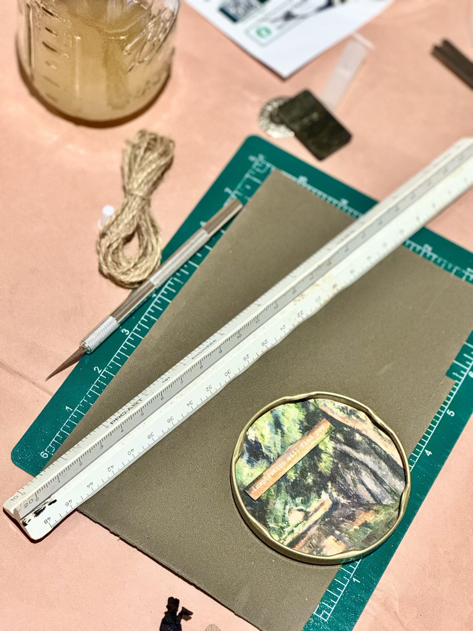The same tin lid in progress on a cutting mat, with a utility knife, a triangular ruler, and twine.